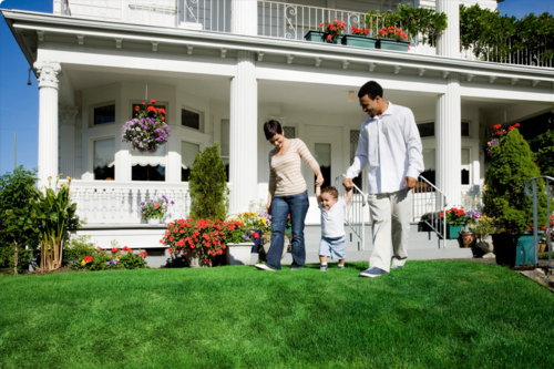 A photo of a family walking on a luscious green lawn in front of a beautiful white house.